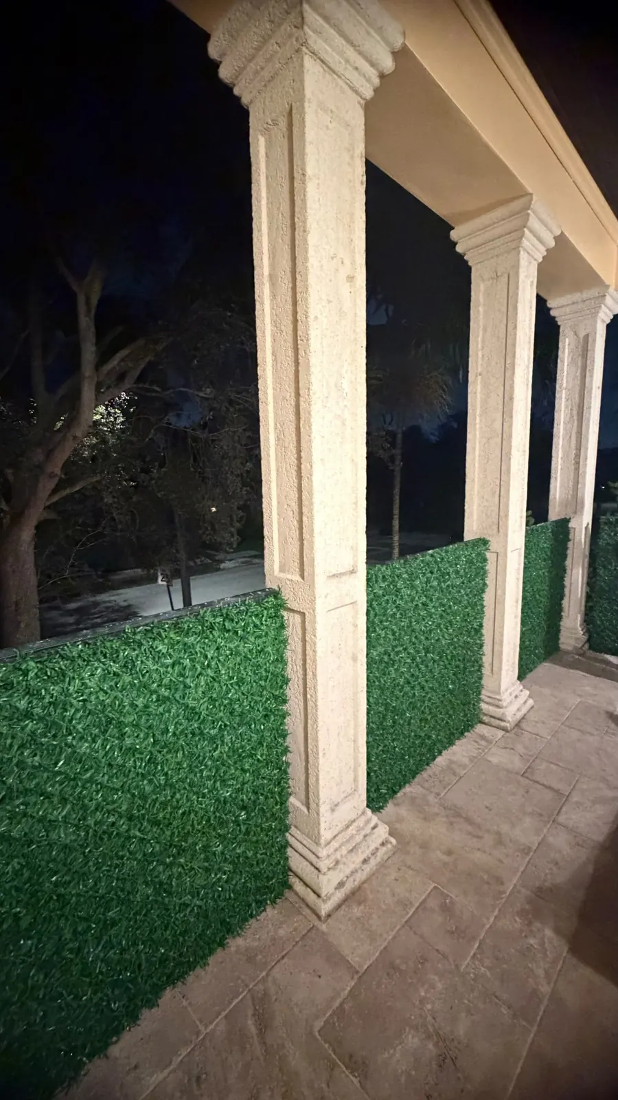 Balcony columns wrapped in Dolce Green grass fence panels at night