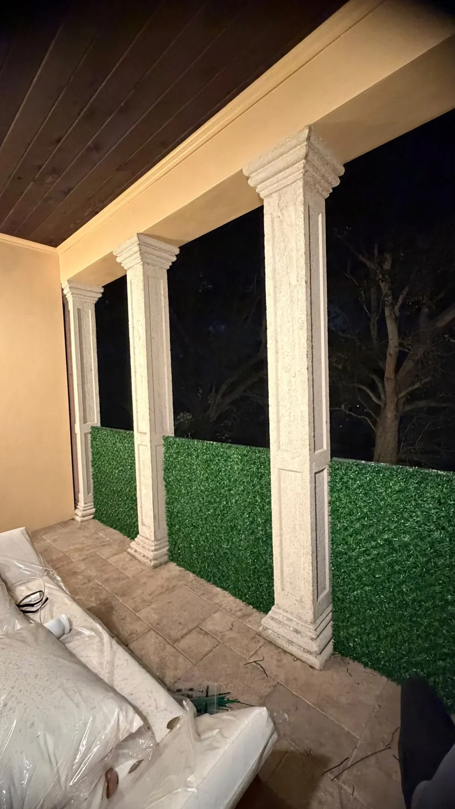 Balcony columns wrapped in Dolce Green grass fence panels at night